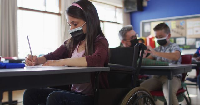 Children wearing face masks are studying in an inclusive classroom, promoting an environment of diversity and learning. The image emphasizes education during the pandemic and highlights the inclusion of children with disabilities. This image is suitable for educational materials, diversity promotion, pandemic-related content, or any content related to inclusive and accessible education systems.
