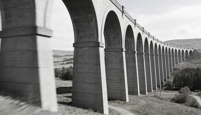 Concrete railway viaduct stretching across rural valley with repeating arches