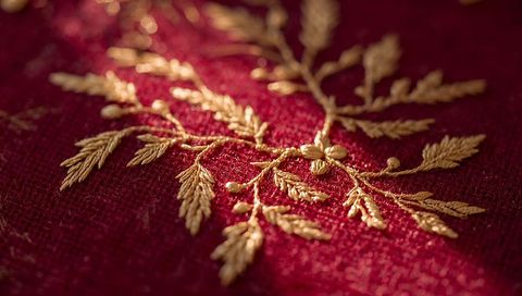 Gold metallic embroidery threadwork close-up on crimson linen macro detail showing ornate botanical