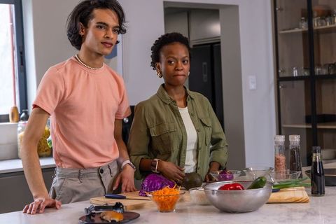 Diverse couple preparing fresh salad and chopping vegetables at modern kitchen island