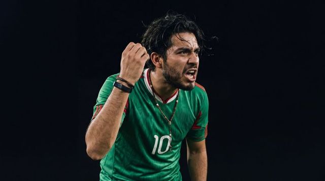 Shouting soccer player raising right fist wearing green no10 jersey under dramatic stadium lights
