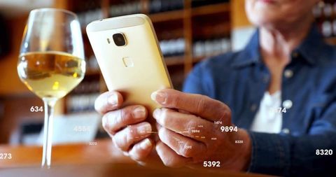 Senior Woman Using Smartphone with White Wine in Elegant Bar