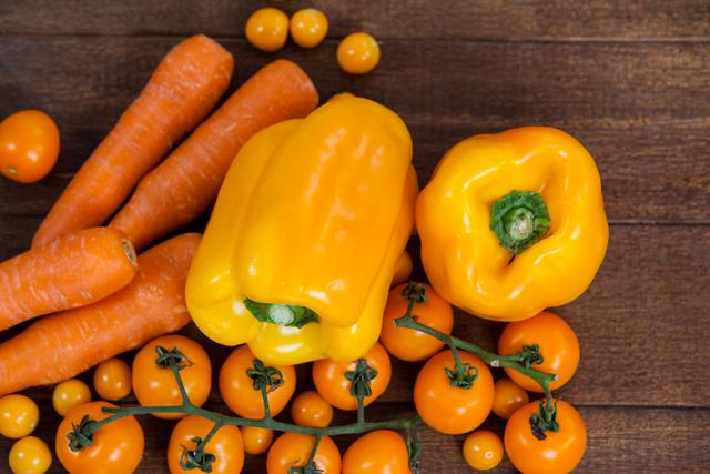This vibrant arrangement of fresh yellow bell peppers, carrots, and cherry tomatoes on a wooden table is perfect for promoting healthy eating, diet plans, and organic produce. Ideal for use in food blogs, nutrition articles, and advertisements for farmers' markets or grocery stores.