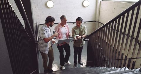 Diverse Team Collaborating on Office Stairs with Laptop and Smartphones