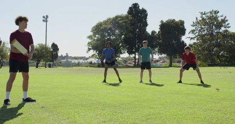 Multiracial friends practicing cricket batting and fielding in sunny park