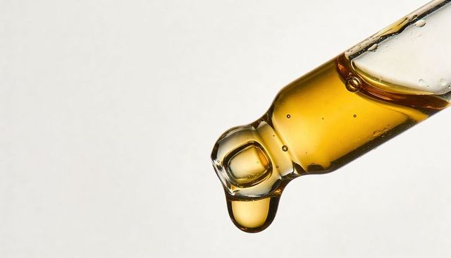Golden serum droplet forming on glass dropper macro for skincare and beauty branding