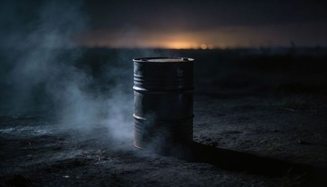 Smoldering Rusted Oil Drum Releasing Smoke on Barren Dirt Lot at Night