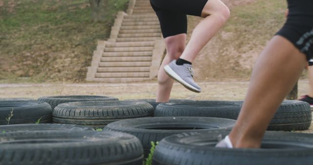 Low section of two caucasian women running through tyres at bootcamp training. Female fitness, friendship, challenge and healthy lifestyle.