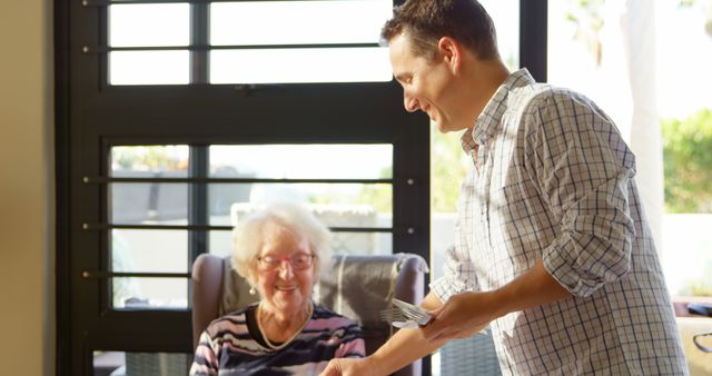 Smiling Young Man Serving Meal to Elderly Woman in Bright Home - Download Free Stock Images Pikwizard.com