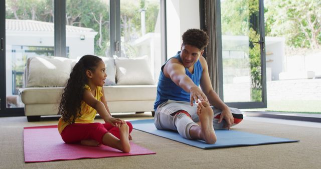 A father and daughter are stretching on yoga mats indoors. They are both engaged in a yoga practice session in a bright living room. This image can be used for promoting family-oriented fitness programs, home workout apps, or healthy lifestyle campaigns. Ideal for illustrating the importance of spending quality time with children while staying active and fit.