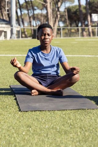 African-american teen meditating on yoga mat outdoors on sunlit turf for mindfulness focus