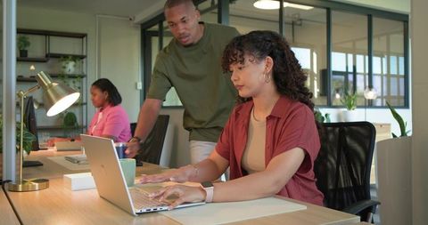 Diverse coworkers collaborating at shared desk in modern open-plan coworking office