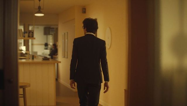 Businessman walking down office corridor toward reception desk in warm ambient lighting