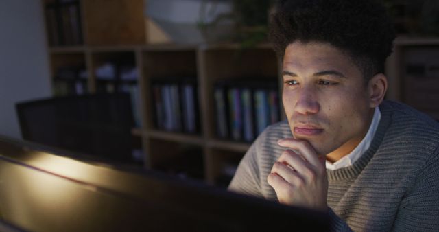 Image of focused biracial man using computer, working late in office. Business and working in office at night with technology concept.