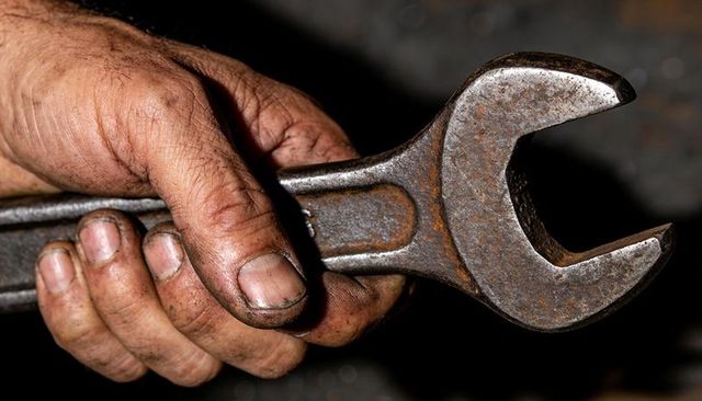 Callused mechanic hand gripping rusted open-end wrench close-up gritty workshop repair