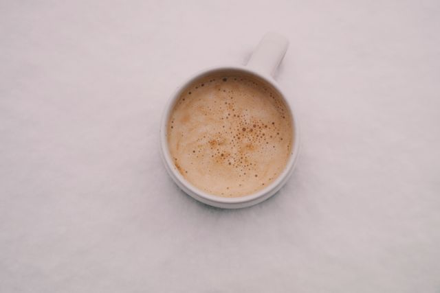 Coffee cup with frothy coffee placed on pristine snow creates a stark contrast between the hot drink and cold snow. Useful for winter-themed content, advertisements for coffee shops, and imagery related to warmth in cold settings. Ideal for social media posts, blogs about winter activities, or presentations on minimalism and contrast.