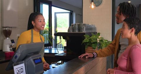 Friendly barista serving couple at rustic coffee counter with qr code terminal and espresso