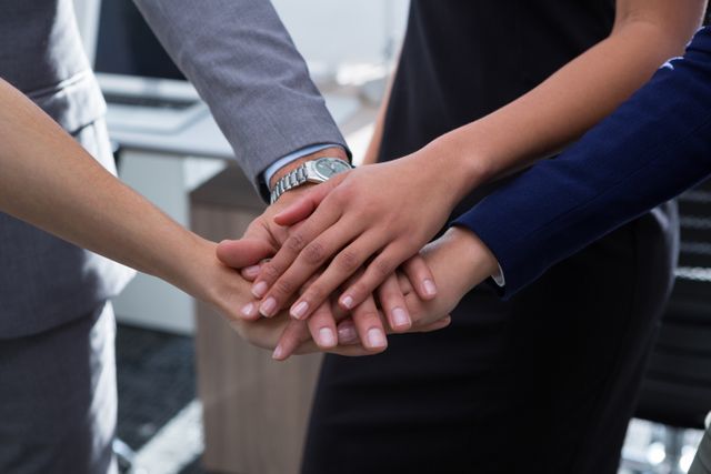 This image shows a close-up of a group of business executives stacking their hands together, symbolizing teamwork and unity. It is ideal for use in corporate presentations, team-building workshops, motivational materials, and business websites to emphasize the importance of collaboration and mutual support in achieving success.
