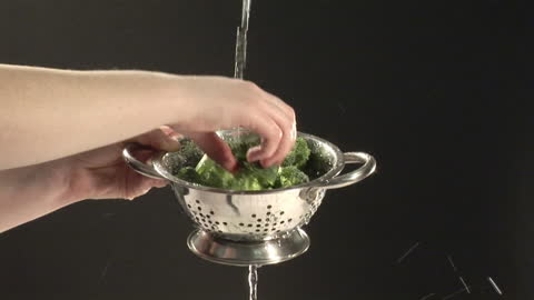 Hands Rinsing Fresh Broccoli in Stainless Steel Colander