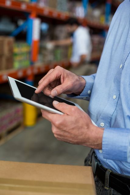 Mid section of warehouse worker using digital tablet in warehouse
