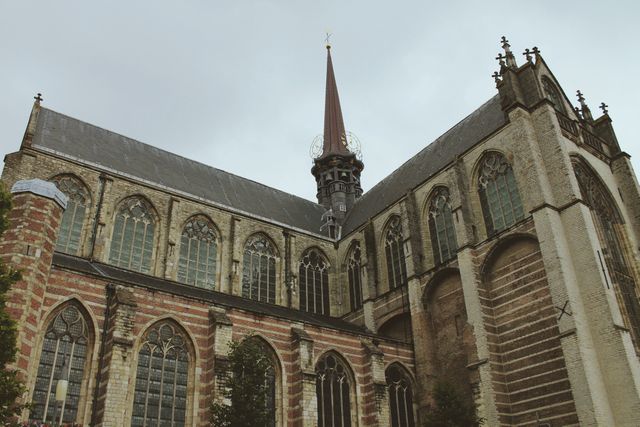 Gothic church exterior featuring arched windows and a tall, intricate spire, photographed on a cloudy day. Highlights medieval architecture and historical significance. Useful for themes related to religion, history, architecture, travel, and European landmarks.