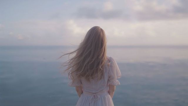 Woman in White Dress Facing Tranquil Sea at Calm Shoreline
