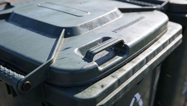 Glinting sunlight revealing stacked green-gray recycling bin lids with hinge scratches