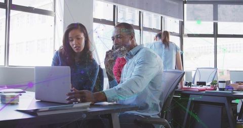 Business team collaborating over laptop in open-plan office with digital network overlay