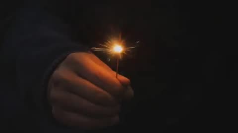 Hand Holding Sparkler at Night Closeup Showing Warm Glow and Flying Sparks