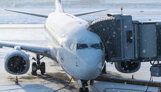 Snow-covered narrow-body jet docking at gate with jet bridge on winter airport ramp