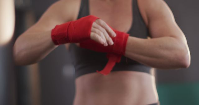 Woman wrapping her hands with red boxing bandages in a gym. Ideal for fitness and sports-related content, promoting physical exercise, boxing training, and strength workouts. Suitable for motivational and athletic themes.