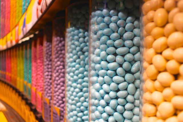 Vibrant display of various colored candies in clear dispensers found in a candy shop. Ideal for use in advertisements for confectionery stores, blog posts about sweets, or background images for party invitations.