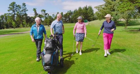 Senior Friends Strolling Golf Course with Gear on Sunny Day