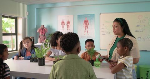 Teacher teaching plant science with elementary students using tablet and potted ferns