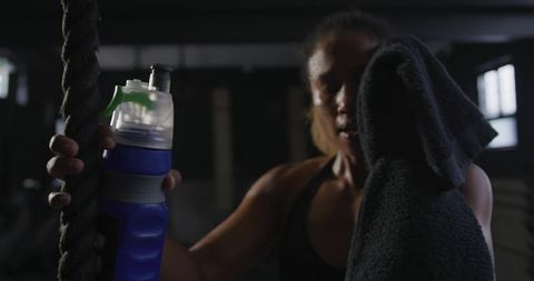 Female athlete resting with water bottle and towel in gym