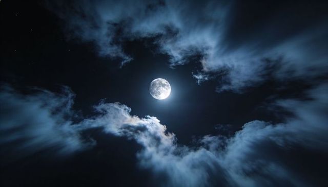 Full moon glowing behind drifting clouds casting blue lunar light across starry night sky