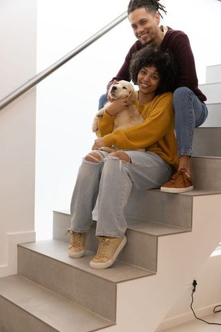 African american couple cuddling puppy while sitting on tiled stairs in cozy home