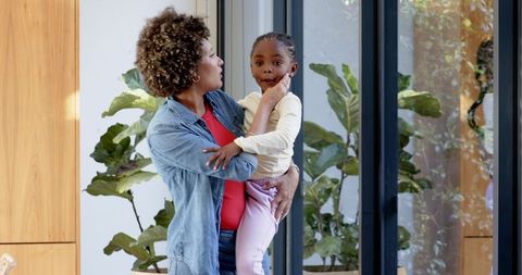 Mother Holding Daughter Near Modern Home Glass Doors