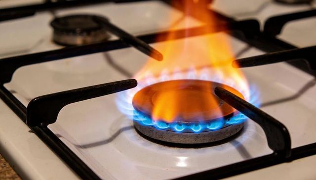 Closeup gas burner flame showing blue ring and orange flame on white cooktop range
