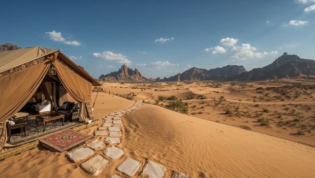 Luxury desert glamping tent revealing rugged mountains and stone path on golden sand dunes