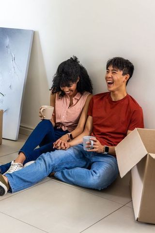 Young diverse couple relaxing while unpacking new home with coffee and cardboard boxes
