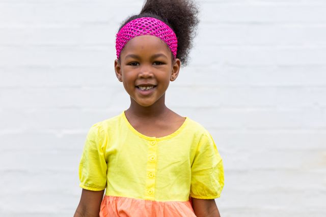 Portrait of happy african american schoolgirl with pink hairband smiling in elementary schoolyard. Education, childhood and learning concept.