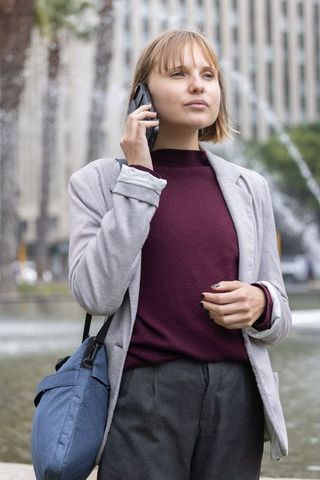Young professional talking on smartphone by urban fountain wearing blazer and shoulder bag