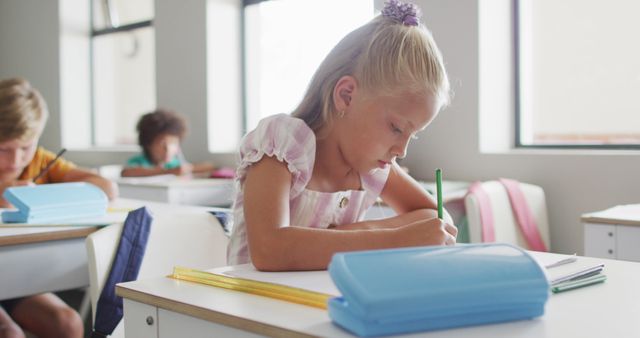 Image of focused caucasian girl sitting at desk in classsroom. primary school education and learning concept.
