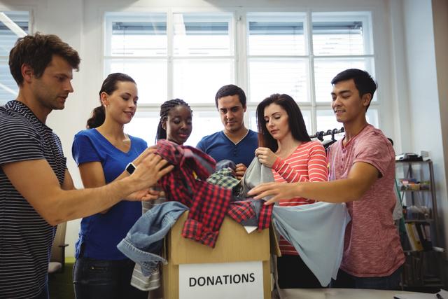 Group of diverse volunteers sorting through donated clothes in a community center. Ideal for illustrating community service, charity work, teamwork, and social responsibility. Useful for nonprofit organizations, volunteer recruitment campaigns, and community outreach programs.
