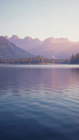 Sunrise painting alpine peaks while lake surface rippling with soft reflections | Vertical video