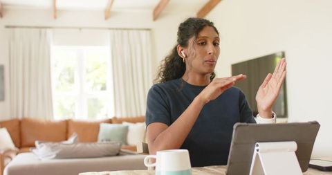 African american woman presenting remotely from home using tablet stand, gesturing during video call