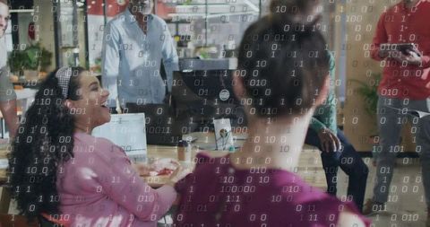 Creative team collaborating around laptops with binary data overlay in modern office