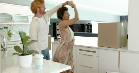 Joyful couple dancing in new kitchen amidst moving boxes