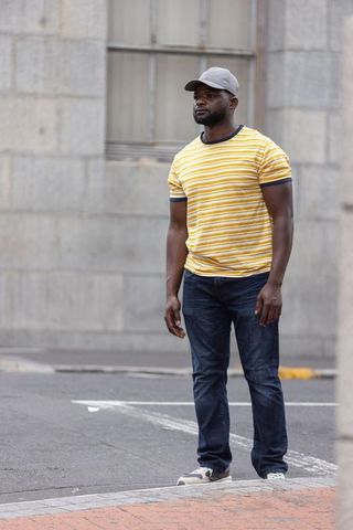 Urban man standing on city sidewalk wearing yellow striped t-shirt and cap casual style